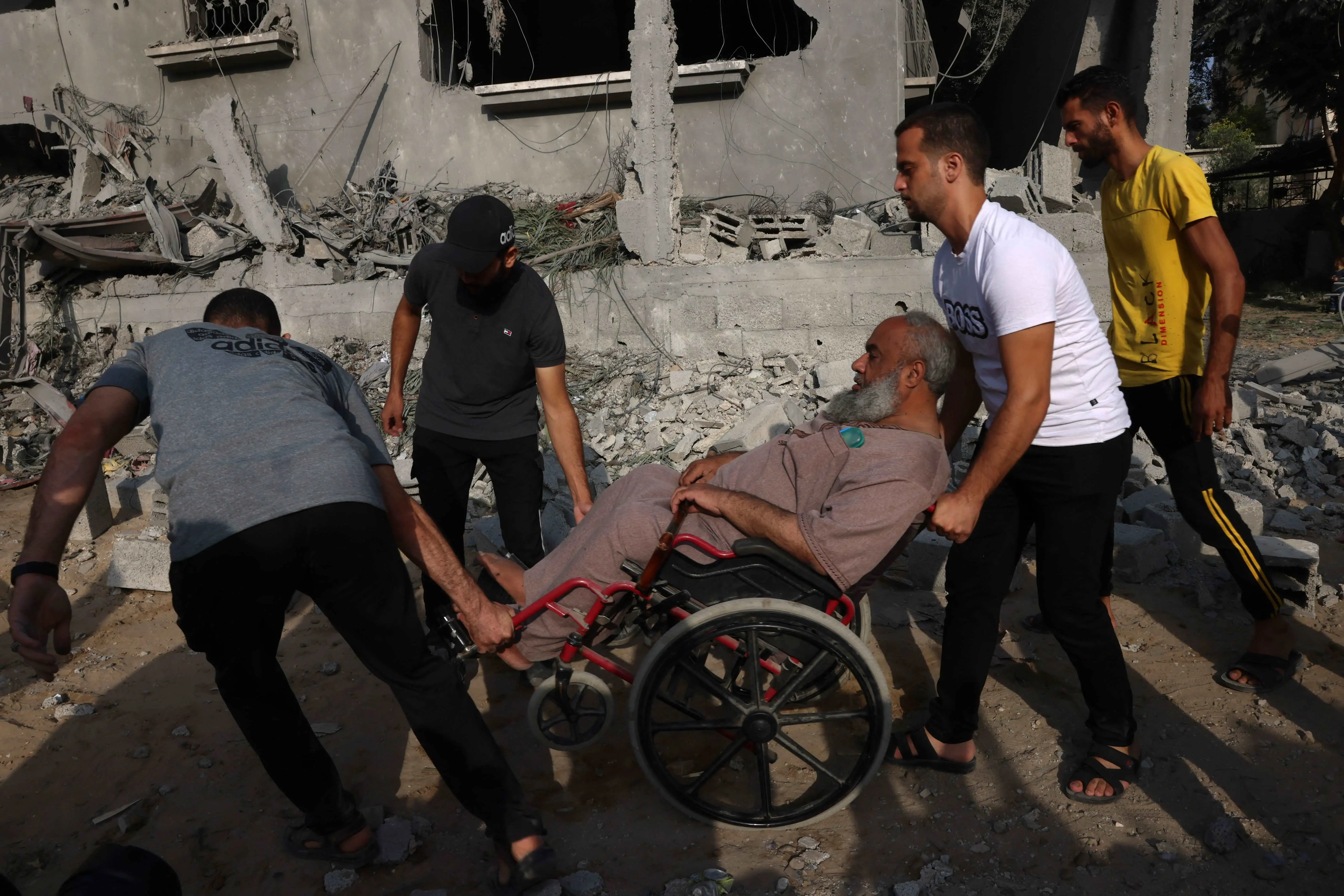 Trois hommes debout aident un homme en fauteuil roulant à se déplacer au milieu des décombres et de la destruction dans le sud de la bande de Gaza le 22 octobre 2023